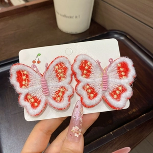 Détail de pinces à cheveux papillon brodées rouge et blanc avec fil doré et glands