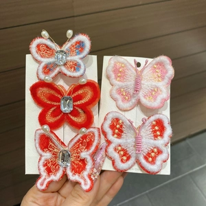 Détail d'une pince à cheveux papillon rouge avec broderie, perles et strass