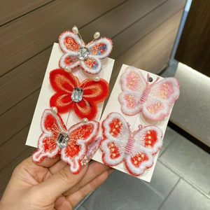 Détail de pinces à cheveux papillon brodées rouge et rose avec perles et strass