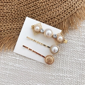 Détail d'un lot de barrettes vintage avec perles et badge doré sur support blanc