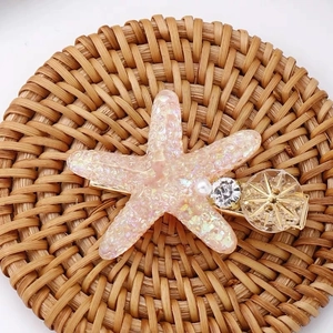 Détail d'une pince à cheveux étoile de mer rose pailletée avec perle et strass