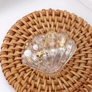 Détail d'une barrette coquillage transparente avec feuilles d'or, perles et un motif étoile