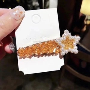 Close-up of star hair clip with amber texture and pearls on a branded card