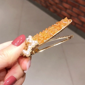 Detail of a golden metal hair clip with amber gravel stones and white pearl accents