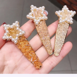 Close-up of three gold star hair clips featuring white pearls and sparkling crystal inlay
