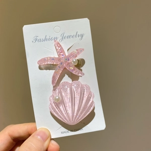 Nahaufnahme von rosa Glitzer-Haarspangen in Seestern- und Muschelform mit Perlen-Details