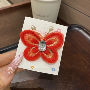 Détail d'une pince à cheveux papillon en résille rouge avec broderie dorée et perles