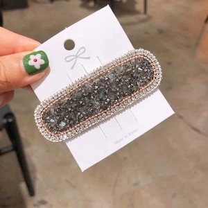 Close-up of a charcoal crystal hair clip with small rhinestones on a display card