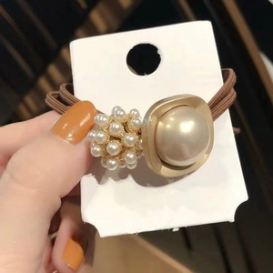 Détail de l'élastique à cheveux marron avec grande perle encadrée d'or et grappe de perles