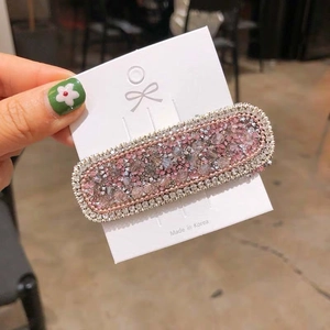 Close-up of a rectangular hair clip with pink and clear crystals on a display card
