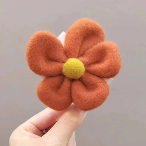 Detailed macro view of orange felt flower hair clip with yellow center and white base
