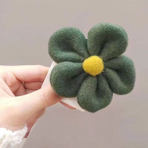 Macro shot of dark green felt flower hair clip with yellow center and wool texture