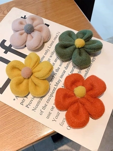 Set of four plush flower hair clips in pink, green, yellow, and orange on a wooden desk
