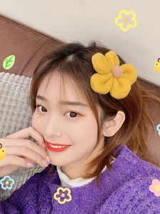 Detailed close-up of a yellow plush floral hair clip with pink center on a female model