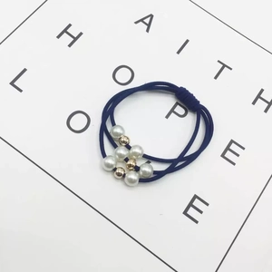 Detail of dark blue elastic hair tie with white pearls and gold beads on card
