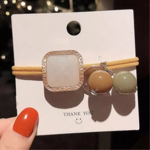Détail d'un chouchou jaune élastique avec un charme nacré carré et des perles colorées