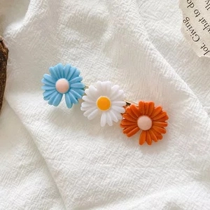 Detailed shot of cute resin daisy hair clips in blue, white, and orange on fabric