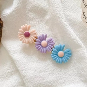 Detailed view of three pastel daisy hair clips on soft fabric, featuring golden metal bases