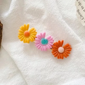 Detailed macro view of three resin daisy hair clips in candy colors on white fabric