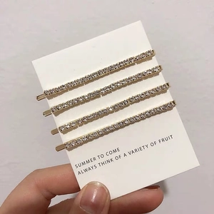 Detailed view of four golden hair clips with sparkling white rhinestones on card