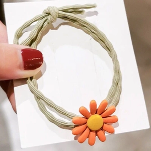 Detail eines hellgrünen Haargummis mit orangefarbenem Gänseblümchen auf Trägerkarte