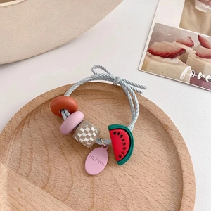 Detailaufnahme von blauem Haargummi mit Wassermelone-Anhänger und Perlen auf Holztablett