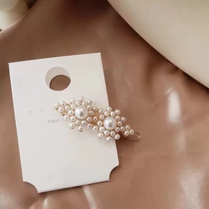 Detail of two pearl flower hair clips on white card over coffee silk background