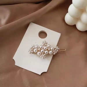 Elegant pearl hair clip with gold metal base and white beads on brown satin fabric