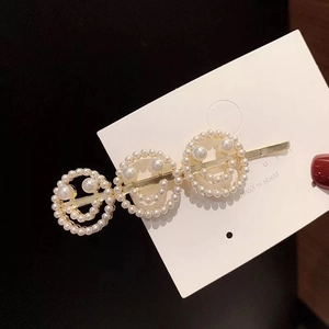 Detail showing three pearl smileys on a golden hair clip against a dark background
