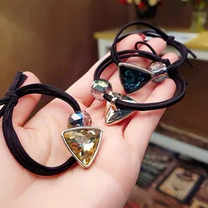 Detailed view of three elastic hair ties with faceted triangular crystal pendants in the hand