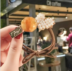 Detail of handmade elastic hair tie featuring pearl heart charm and amber bead accessory