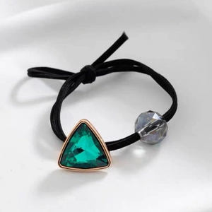 Detail of high-elastic black hair tie with green crystal triangle and gold metal frame