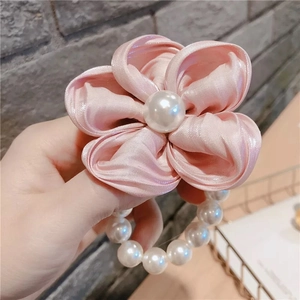 Gros plan d'une pince à cheveux fleur en satin rose avec perle centrale et perles enfilées