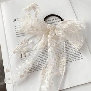 Elegant white lace bow hair clip with intricate floral embroidery on a soft background