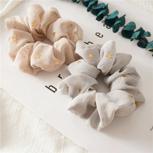 Set of two chiffon scrunchies in beige and grey with gold star patterns on a white background