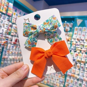 Détail de deux barrettes à nœuds en tissu faits main en orange et imprimé fleuri sur carte