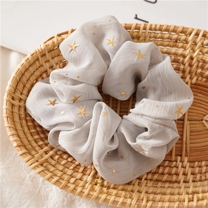 Detailed shot of grey chiffon scrunchie with gold star pattern in a woven basket