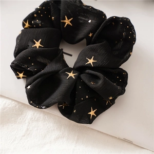 Detailed view of black chiffon scrunchie with shiny gold star prints and star dust accents
