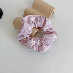 Detail of light pink daisy print scrunchie with soft ruffled fabric texture and elastic