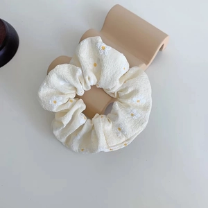 Detailed macro of a cream floral scrunchie with daisy prints on soft fabric