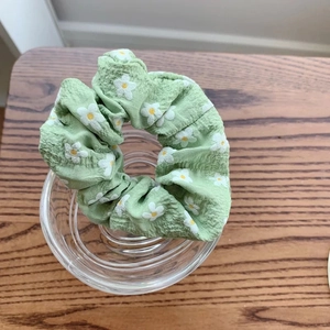 Detailed close-up of light green floral scrunchie with daisy prints on wooden surface