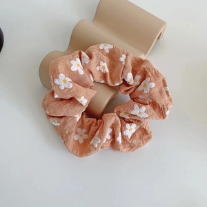 Close-up of pink-orange fabric scrunchie with white daisy embroidery on a stand