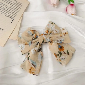 Gros plan d'une pince à cheveux nœud en mousseline fleurie avec motifs orange