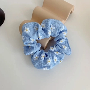 Close-up of light blue floral scrunchie with white daisy pattern on wavy display stand
