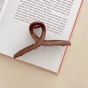 Vue détaillée d'une grande pince à cheveux marron café brillante sur un fond de livre esthétique
