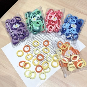 Set of colorful elastic hair ties in transparent daisy-themed packaging on wood background