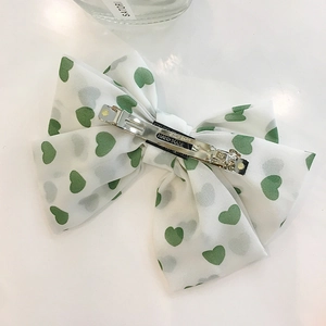 White double-layered satin bow hair clip with green hearts and a silver spring fastener