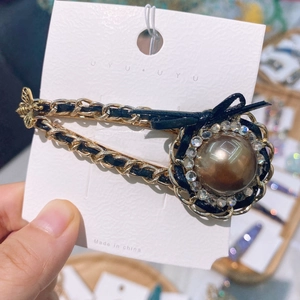 Detail of vintage hair clip with gold chain, black leather weave and a large pearl