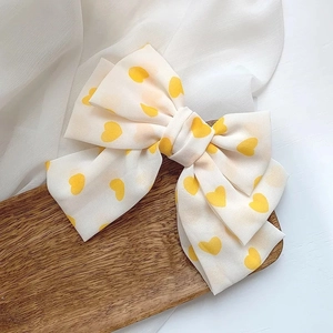 Detail of soft cream oversized bow hair clip with yellow heart prints on satin fabric