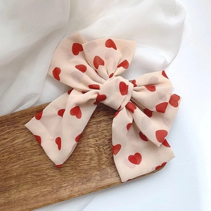 Detail of a beige double-layered satin bow hair clip with red heart patterns on silk